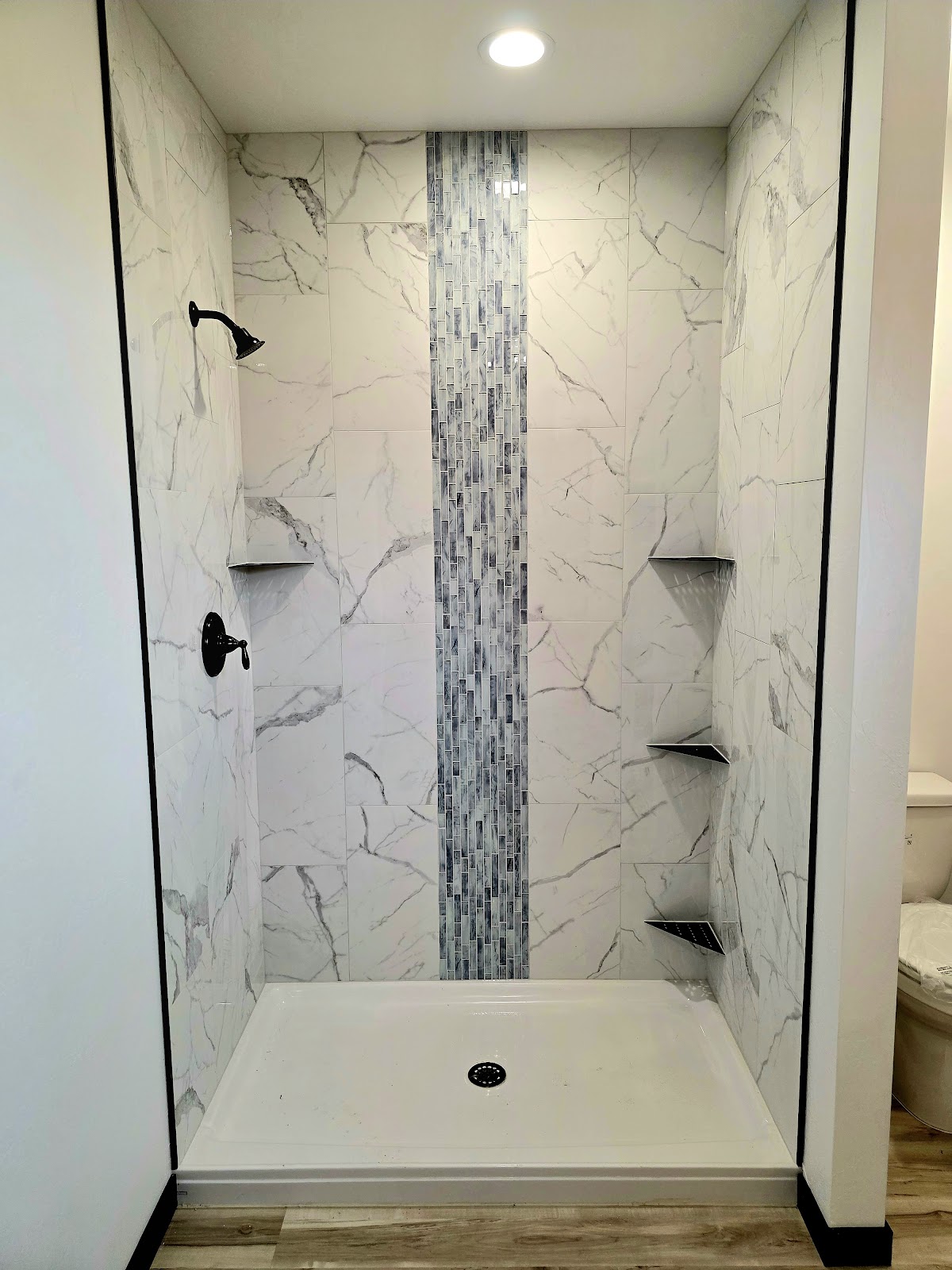 White marble-look tile shower with blue glass mosaic stripe